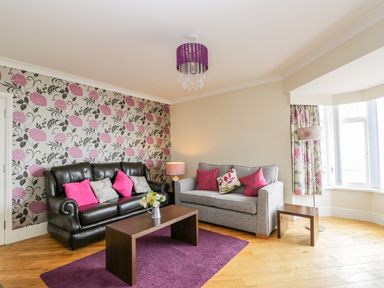 A living room with two sofas a wooden coffee table purple rug floral wallpaper and window with curtains at The Gansey Girl in Bridlington