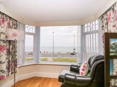 A sitting area with a black leather armchair a floor lamp and floral curtains overlooking the sea at The Gansey Girl in Bridlington