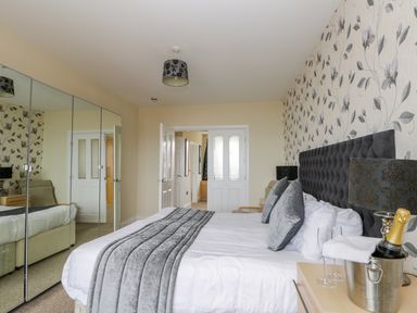 A bedroom with a bed with gray pillows and blanket next to a bedside table with a lamp and champagne bucket at The Gansey Girl in Bridlington