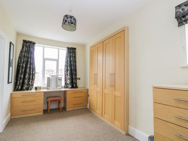 A room with wooden wardrobes and drawers a window with curtains and a small stool at The Gansey Girl in Bridlington