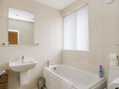 A bathroom with a bathtub a sink a mirror a window with blinds and a toilet at The Gansey Girl in Bridlington