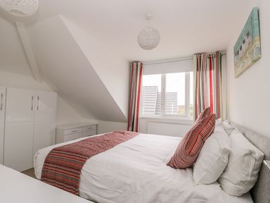 A bedroom with a bed with striped pillows and bed runner near a window with striped curtains and a white wardrobe at The Gansey Girl in Bridlington