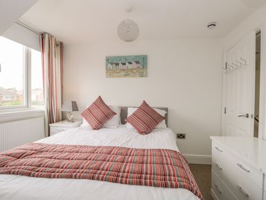 A bedroom with a bed with striped pillows and blanket a bedside table and chest of drawers at The Gansey Girl in Bridlington