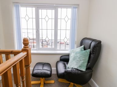 A black leather armchair with a footrest and two green cushions next to a window with a wooden railing at The Gansey Girl in Bridlington