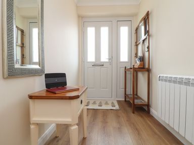 A hallway with a white side table holding a router and book and wooden coat rack near a white door at Tremethic in Trewoon