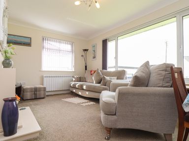 A living room with two beige sofas a wooden chair a window with vertical blinds and a purple vase on a shelf at Tremethic in Trewoon