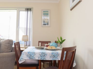 A dining table with a blue floral tablecloth set with plates teapot scones and a vase with flowers in a room with a window and a lamp at Tremethic in Trewoon