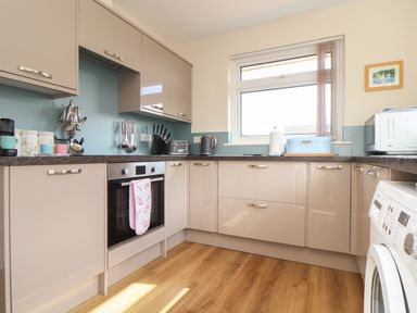 A kitchen with beige cabinets and drawers a built in oven a washing machine and countertop appliances at Tremethic in Trewoon