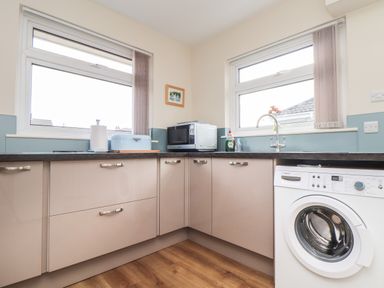 A kitchen with beige cabinets a washing machine a microwave sink and two windows at Tremethic in Trewoon