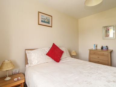 A bedroom with a bed with white bedding and a red pillow bedside tables with lamps a wooden dresser with items and a mirror on the wall at Tremethic in Trewoon