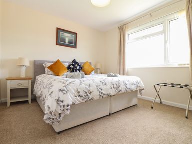 A bedroom with a bed with patterned bedding and pillows bedside tables with lamps a window with curtains and a luggage rack at Tremethic in Trewoon