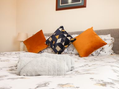 A bed with folded towels and decorative cushions with a lamp on a bedside table at Tremethic in Trewoon