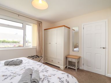 A bedroom with a bed with floral bedding and towels on it a wardrobe a small table with a mirror above and a white door at Tremethic in Trewoon