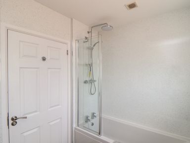 A bathroom with a white door bathtub shower and glass screen at Tremethic in Trewoon