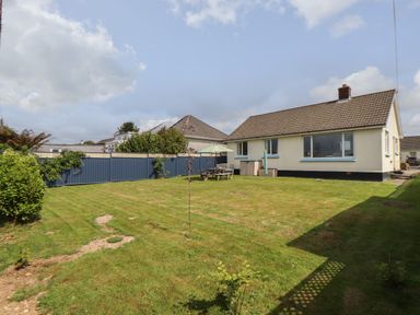 A backyard with a lawn table umbrella and chairs surrounded by a blue fence at Tremethic in Trewoon