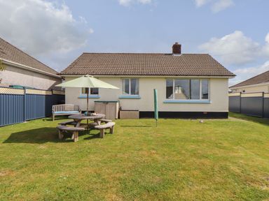 A backyard with a wooden picnic table with umbrella a wooden bench and a cream house with windows a brown tiled roof and chimneypot at Tremethic in Trewoon