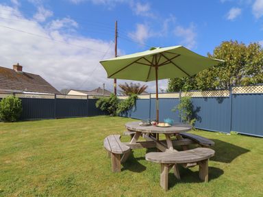 A garden with a round wooden picnic table and green umbrella at Tremethic in Trewoon