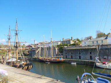 A harbor with several sailing ships docked next to stone buildings and houses at Tremethic in Trewoon