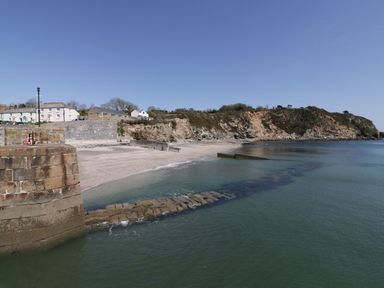 A coastal beach area with stone walls and houses near the shore at Tremethic in Trewoon