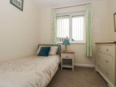 A small bedroom with a single bed a bedside table with lamp a chest of drawers and a window with curtains at Tremethic in Trewoon