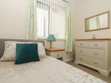A bedroom with a bed side table lamp a chest of drawers and a wall mirror at Tremethic in Trewoon