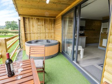 An outdoor patio with a wooden table and chairs a hot tub and a sliding glass door leading to an indoor room at Cilan Lodge in Llandrillo