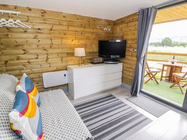 A small room with a couch, cabinet with lamp and TV, rug, and a balcony with wooden table and chairs at Cilan Lodge in Llandrillo