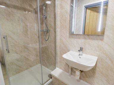 A bathroom with a glass-enclosed shower and a wall-mounted sink with a mirror above it at Cilan Lodge in Llandrillo