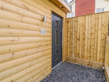 An exterior entrance with a black door next to a wooden wall with a sign reading Cilan Lodge at Llandrillo