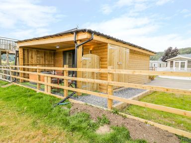 A wooden cabin with a covered porch and outdoor seating behind a wooden fence at Cilan Lodge in Llandrillo