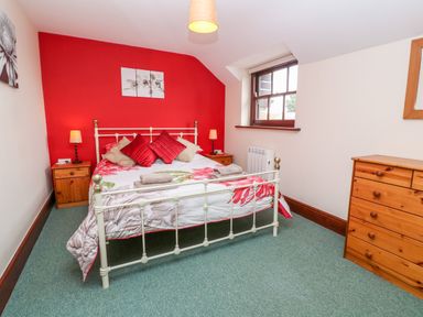 A bedroom with a metal bed frame red accent wall bedside tables and wooden dresser at Mossley Cottage in St Buryan