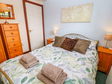 A bedroom with a bed with floral bedding and pillows wooden dressers and lamps on bedside tables at Mossley Cottage in St Buryan