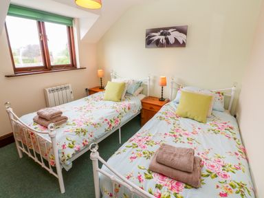 A bedroom with two single beds with floral bedding and green cushions at Mossley Cottage in St Buryan
