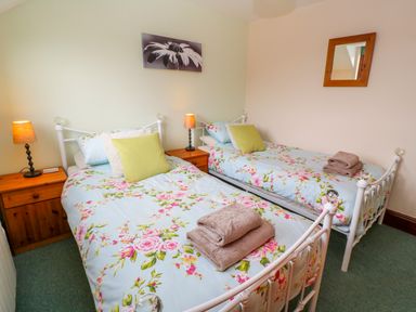 A bedroom with two single beds with floral bedspreads and wooden nightstands with lamps at Mossley Cottage in St Buryan