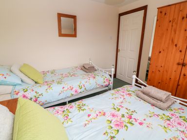 A bedroom with two single beds with floral bedding a wooden wardrobe a wall mirror and a closed door at Mossley Cottage in St Buryan