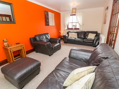 A living room with brown leather sofas and an orange accent wall at Mossley Cottage in St Buryan