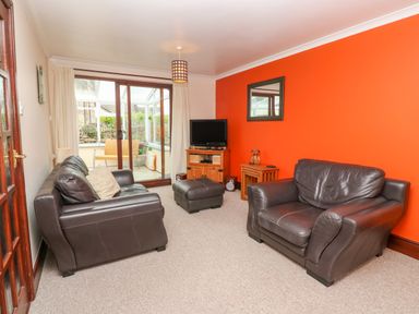 A living room with two leather sofas an ottoman a wooden tv stand with a television and a small wooden side table at Mossley Cottage in St Buryan