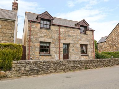Stone house with two dormer windows and a stone wall in front at Mossley Cottage in St Buryan