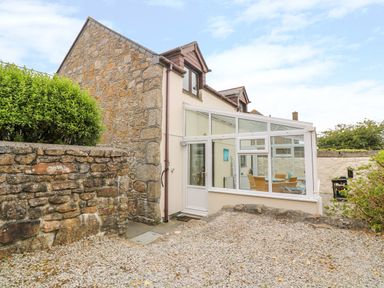 Stone-sided house with a glass conservatory and outdoor gravel area at Mossley Cottage in St Buryan