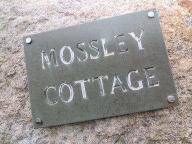 A metal sign with the text mossley cottage mounted on a stone wall at Mossley Cottage in St Buryan