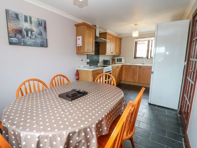 A kitchen with wooden cabinets a white refrigerator a dining table with polka dot tablecloth and wooden chairs at Mossley Cottage in St Buryan