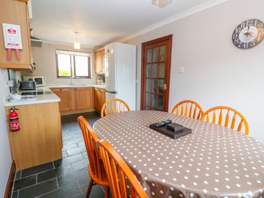 A kitchen with wooden cabinets white refrigerator dining table with polka dot tablecloth and wooden chairs at Mossley Cottage in St Buryan