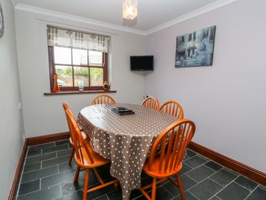 A dining room with a table covered in a polka dot tablecloth surrounded by six wooden chairs at Mossley Cottage in St Buryan