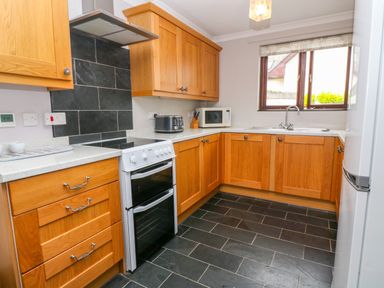 A kitchen with wooden cabinets black tiled floor and a window at Mossley Cottage in St Buryan