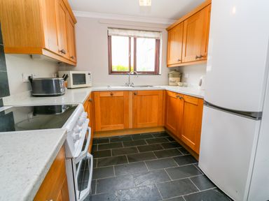 A kitchen with wooden cabinets white appliances and a window at Mossley Cottage in St Buryan