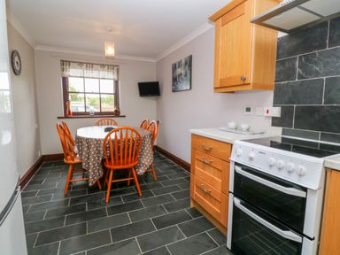 A kitchen with a dining table and chairs a stove and cabinets at Mossley Cottage in St Buryan