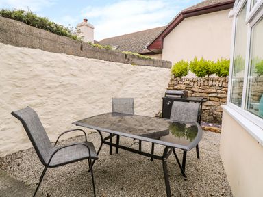 An outdoor seating area with a glass table and three chairs next to a barbecue grill at Mossley Cottage in St Buryan