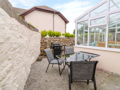An outdoor patio with a glass table and four chairs next to a conservatory at Mossley Cottage in St Buryan