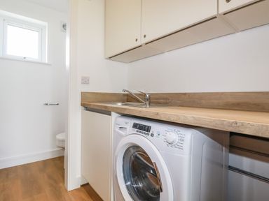 A utility room with a washing machine sink and wooden countertop at Sandpiper in Perranporth