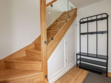 A wooden staircase with a white storage cabinet underneath and a black metal coat rack with shelves at Sandpiper in Perranporth
